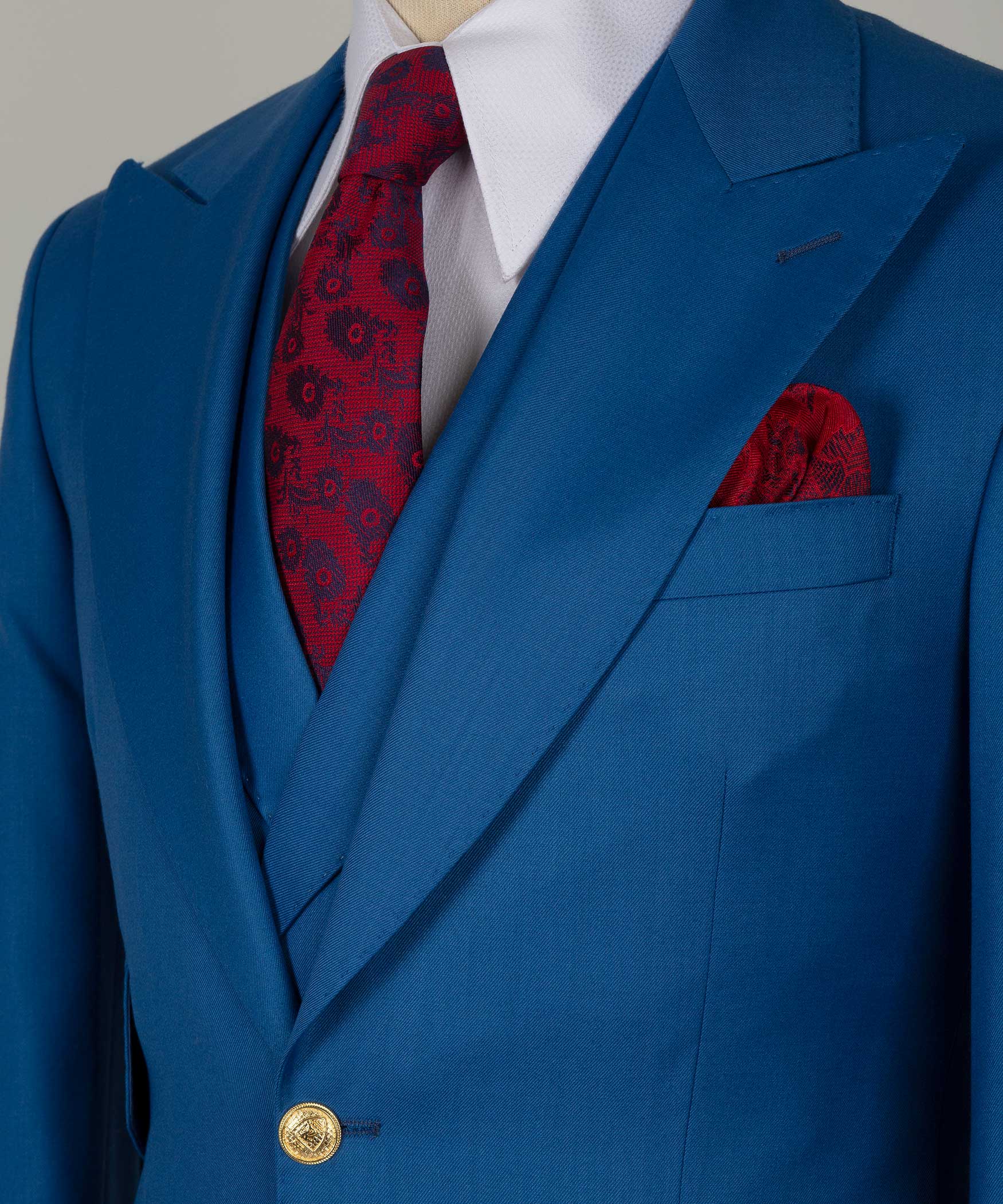 Close-up of blue suit lapel with gold button, red patterned tie, and red pocket square