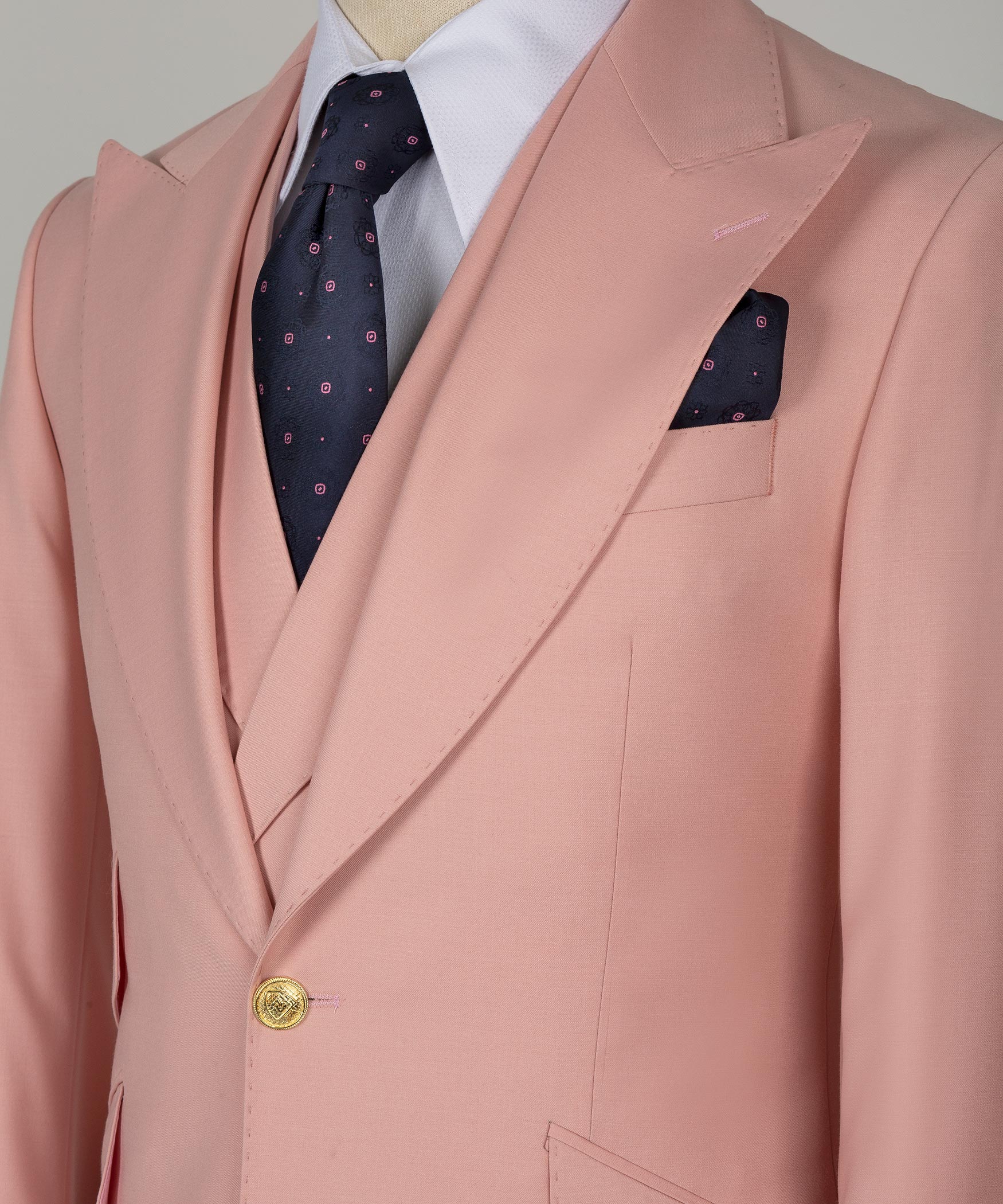 Powder pink suit jacket close-up: gold button, welt pockets, patterned tie