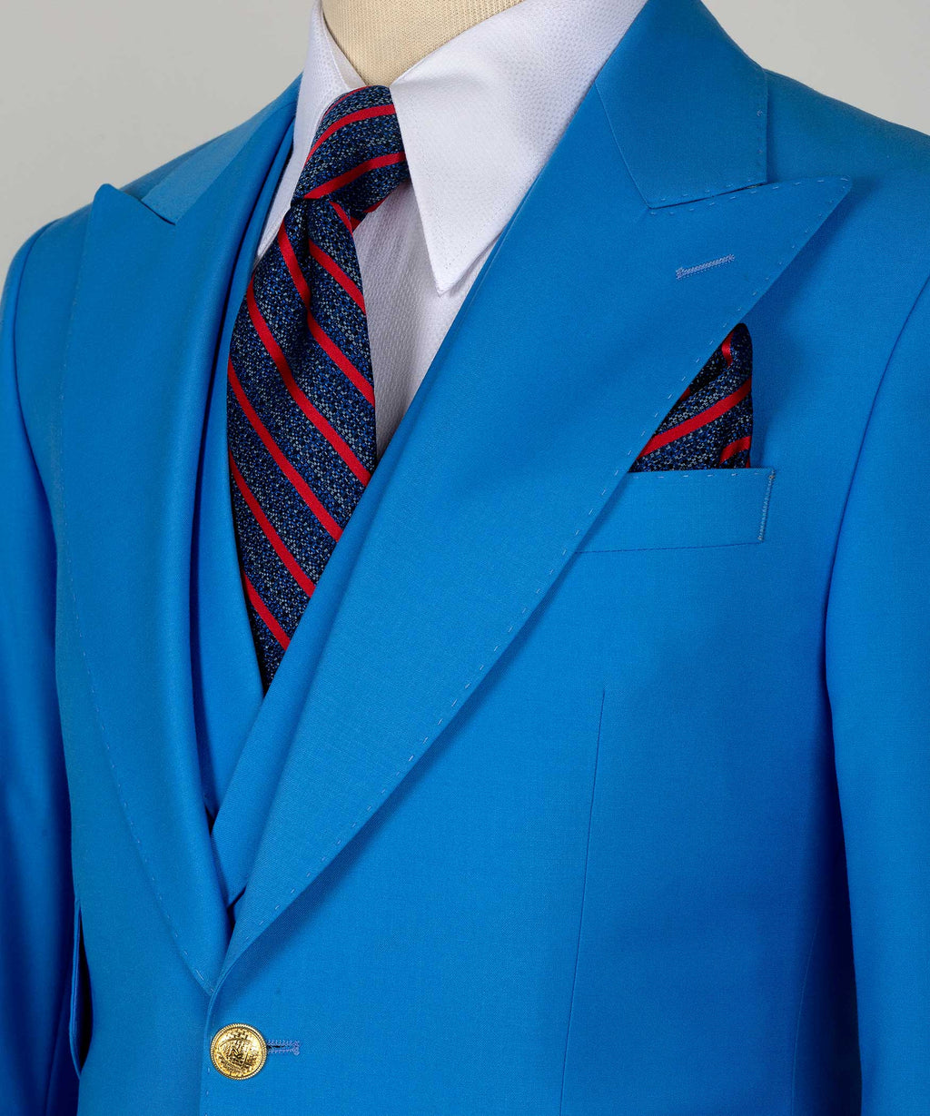 Blue suit jacket lapel detail with gold button and striped tie in red and navy