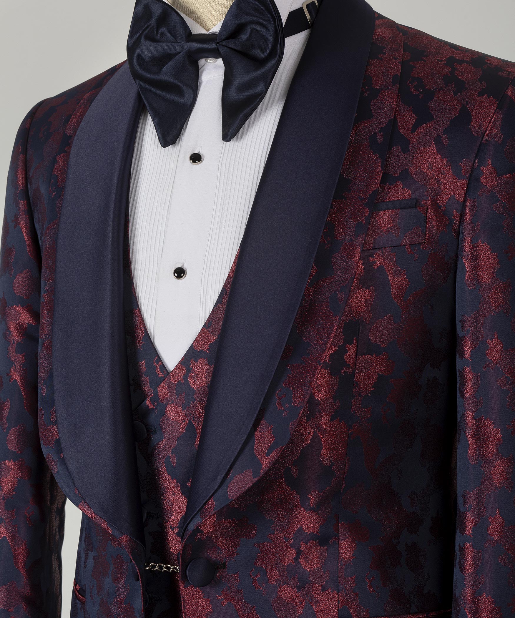 Tuxedo bow tie and dark lapels over burgundy patterned vest, satin sheen