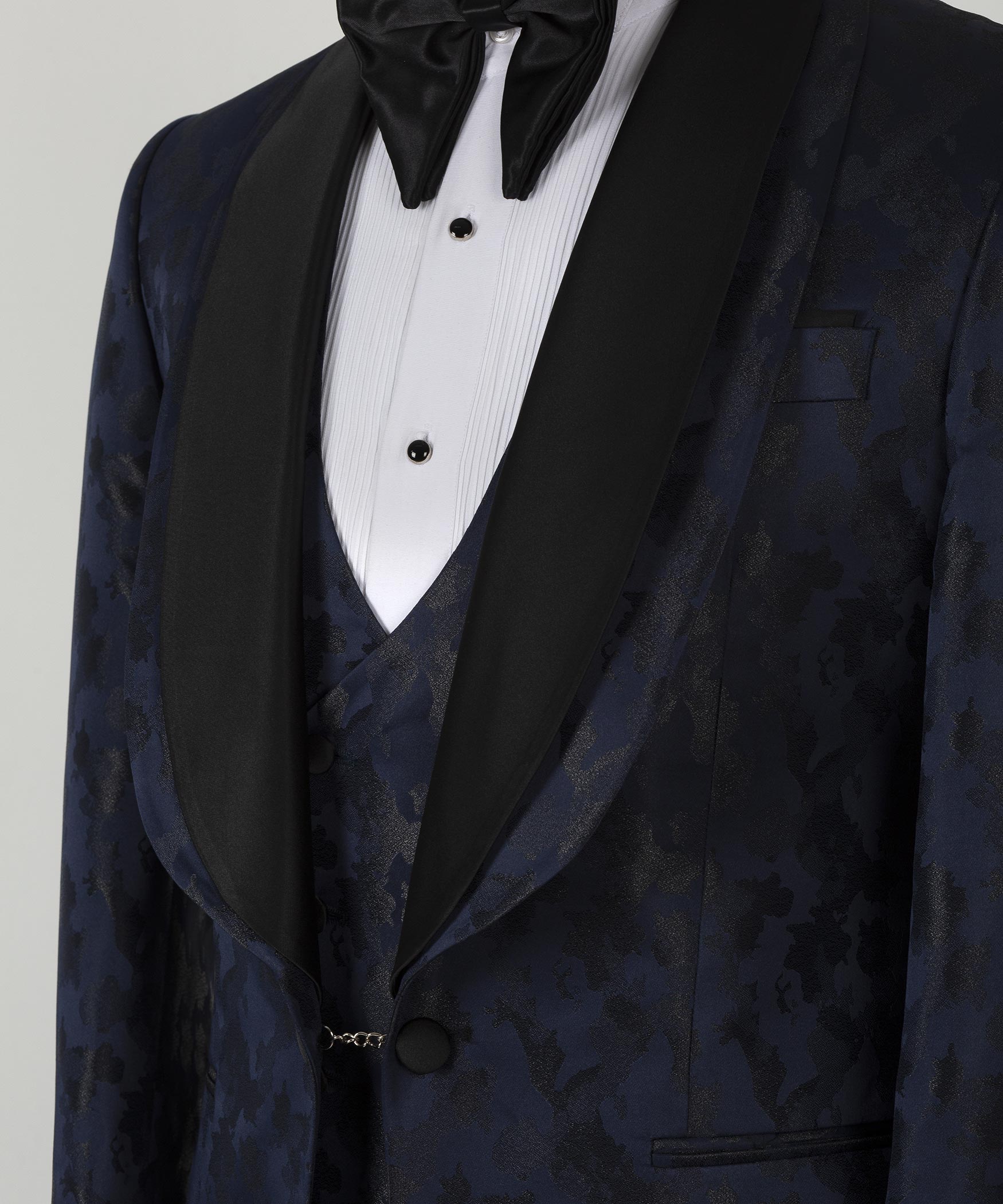 Close-up: navy tuxedo lapels with bow tie and white pleated shirt front, vest with button