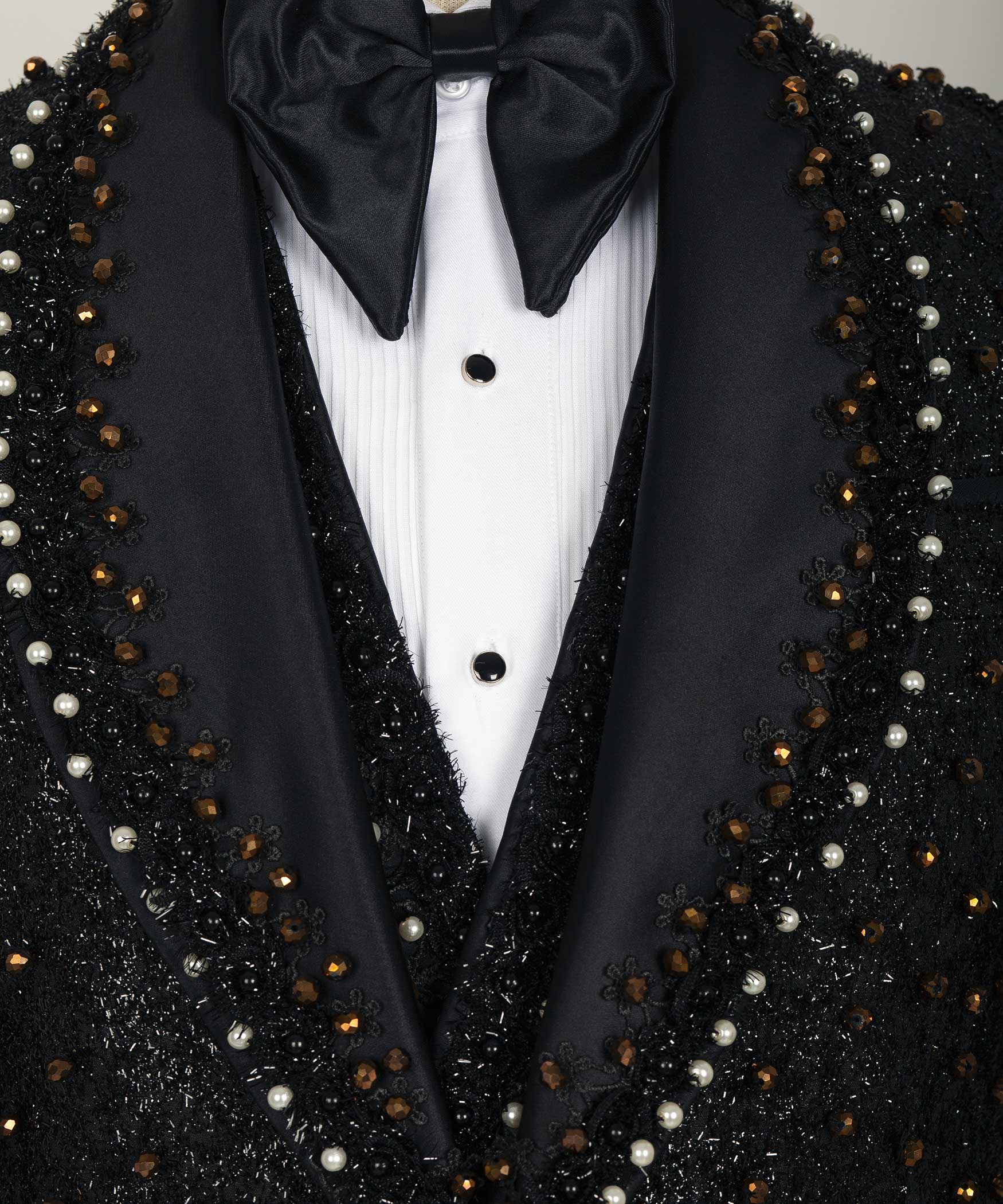 Close-up tuxedo chest: black satin bow tie, white shirt front, and beaded trim
