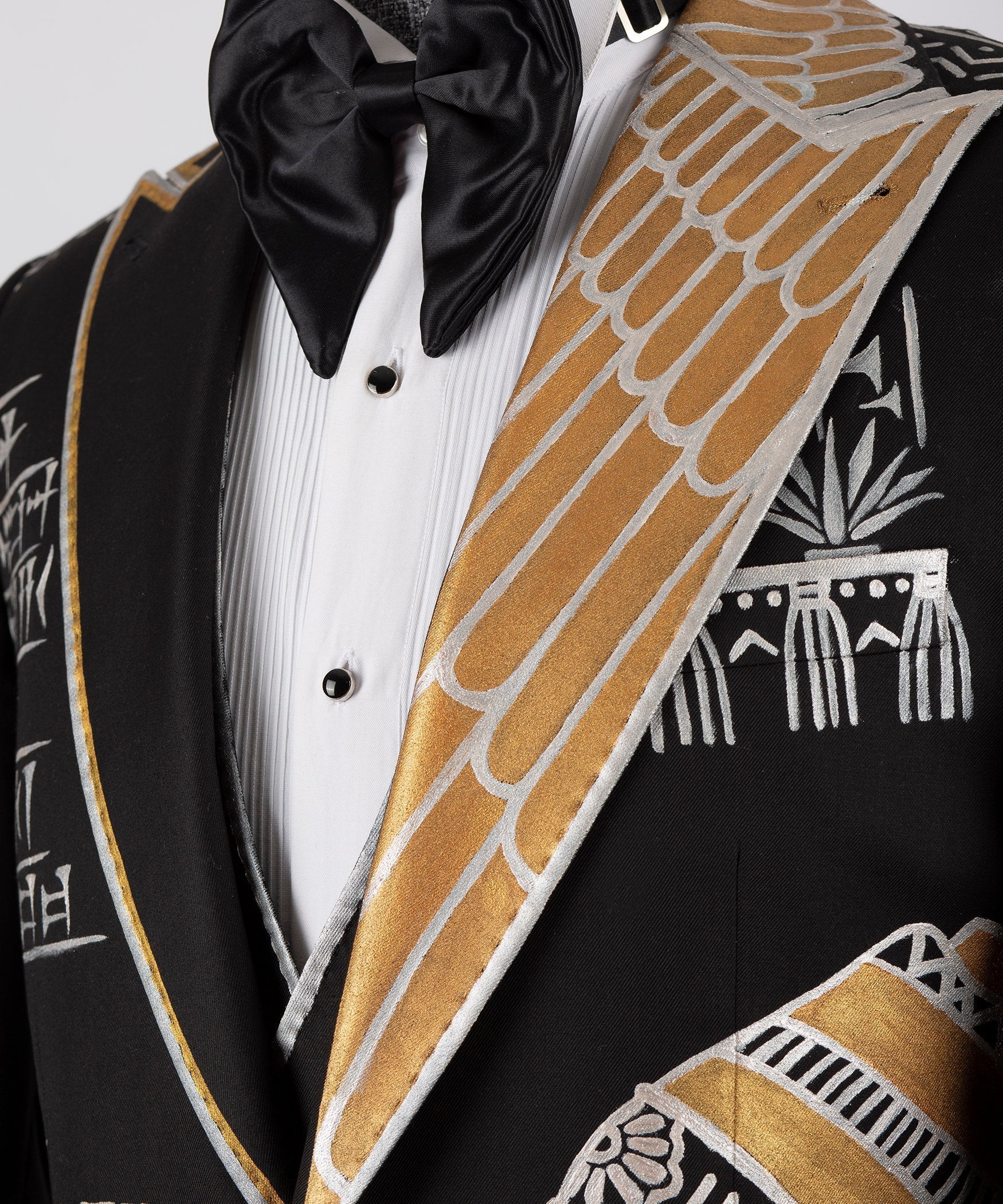 Close-up of black tuxedo lapel with gold embroidered trim, white shirt and bow tie