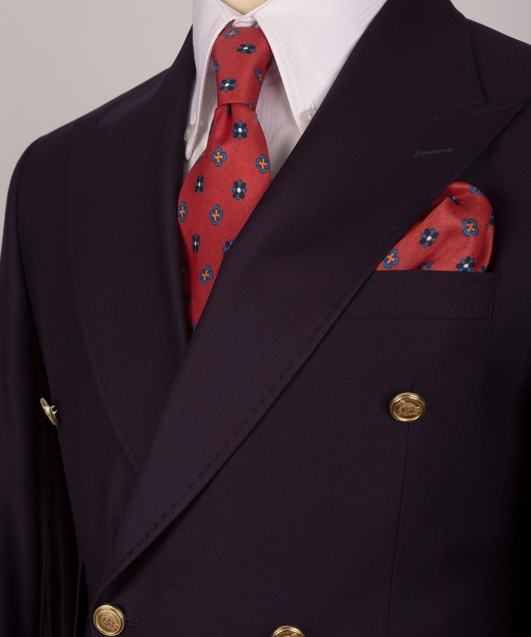 Close-up of dark plum blazer lapel with white shirt, red patterned tie, and pocket square