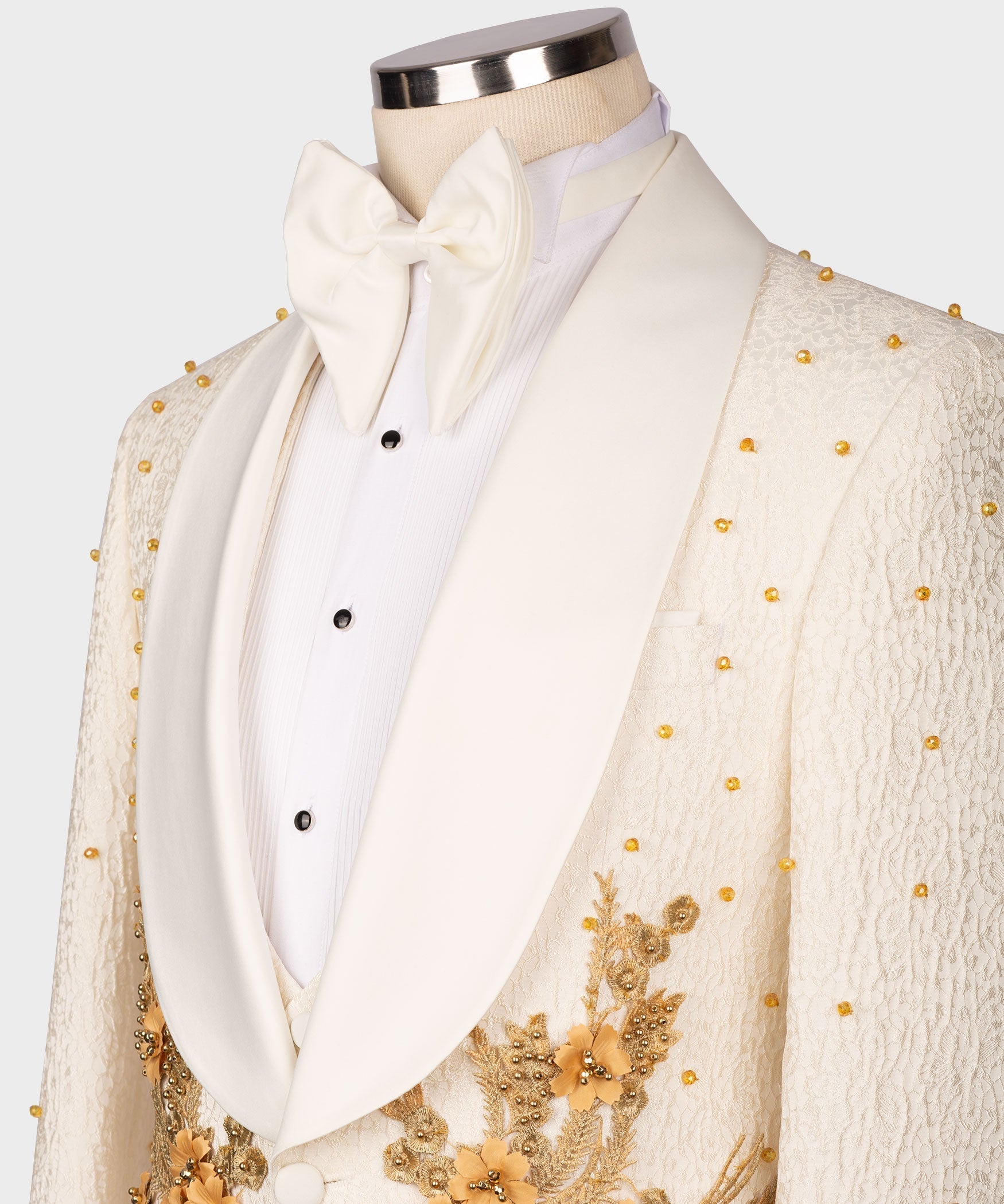Cream tuxedo set detail: white bow tie, buttoned waistcoat, gold-embroidered jacket