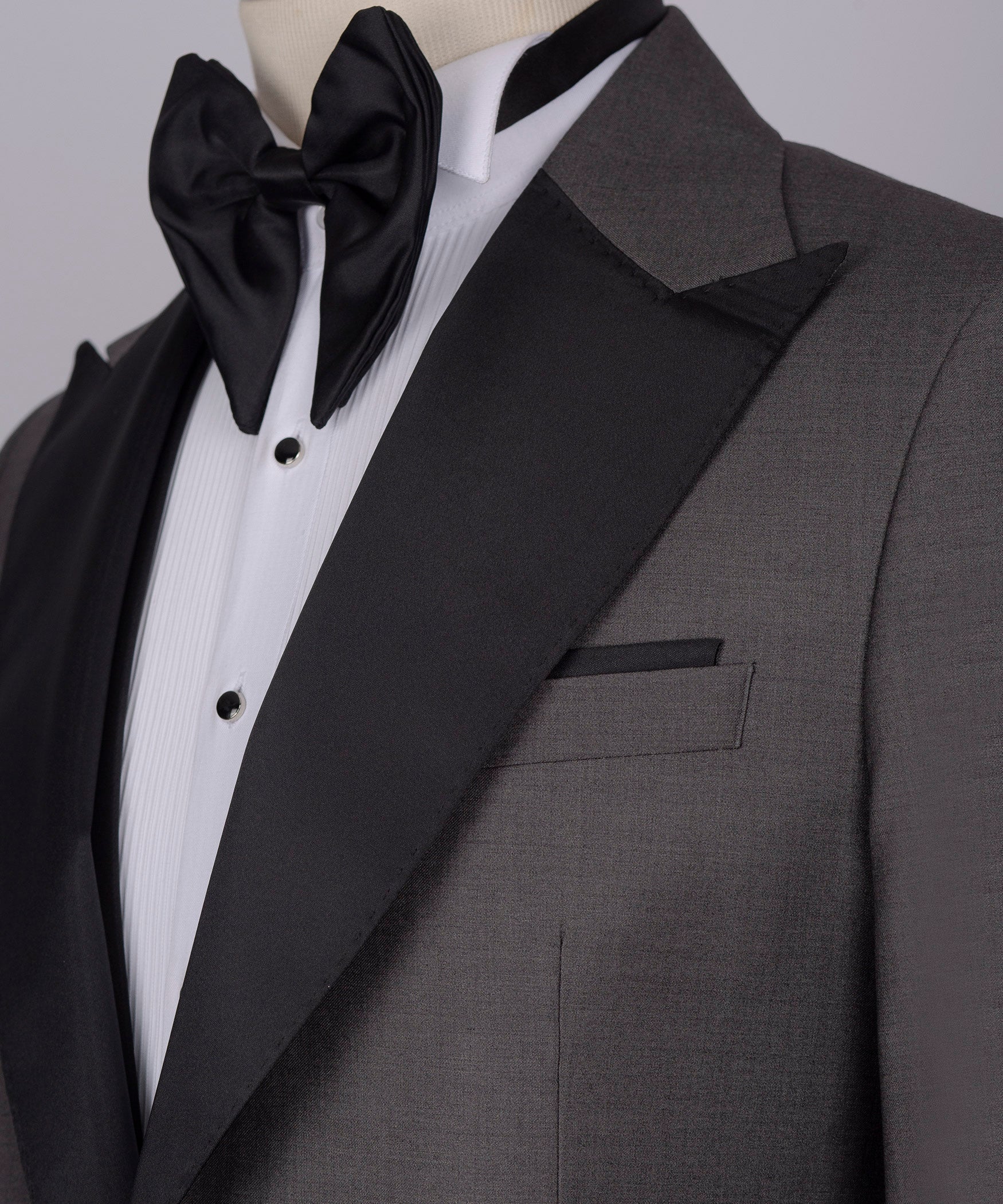 Black bow tie, white striped shirt, and charcoal tuxedo jacket lapel with pocket detail
