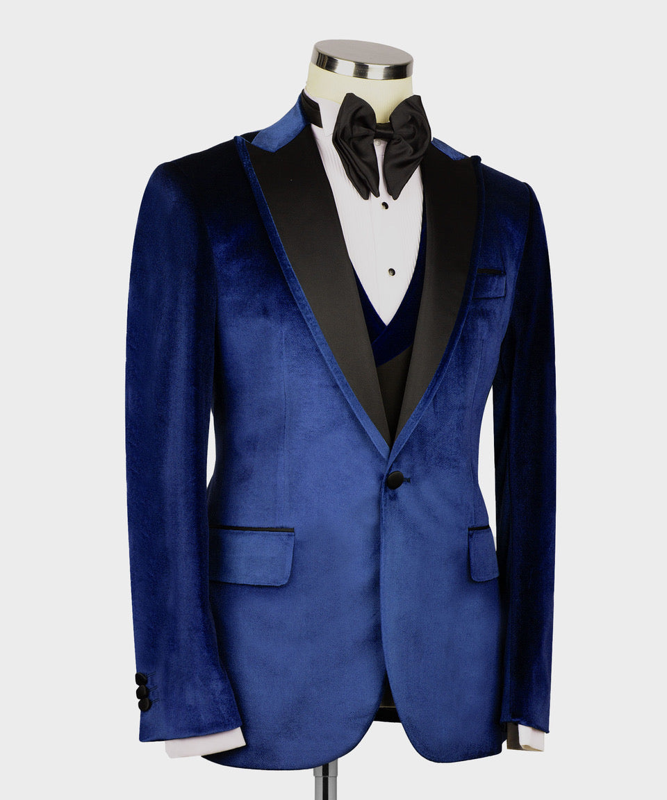 Blue velvet tuxedo jacket angled view with satin-trim lapels, vest, and black bow tie