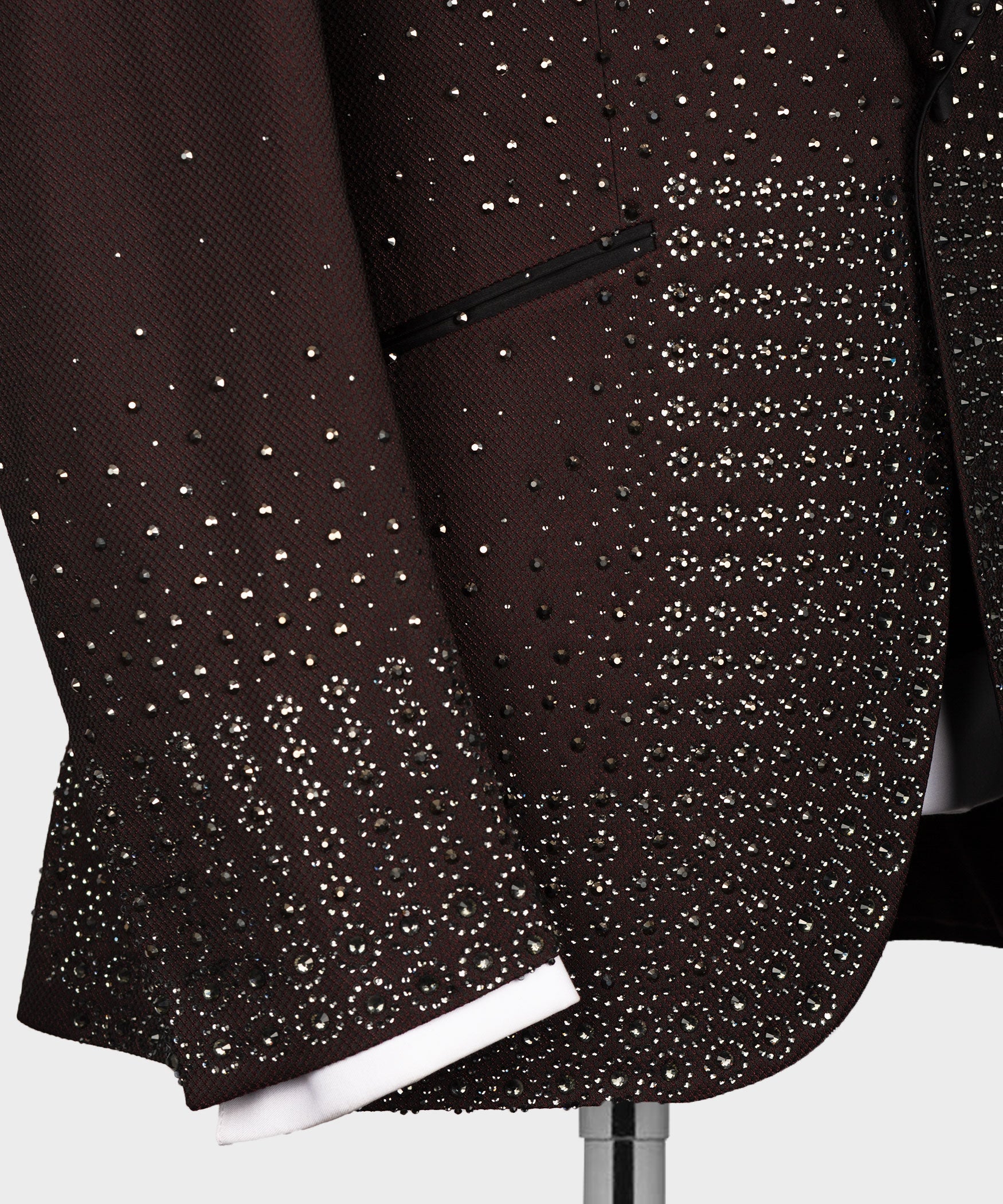 Close-up of burgundy tuxedo jacket hem with dense jeweled pattern and decorative trim
