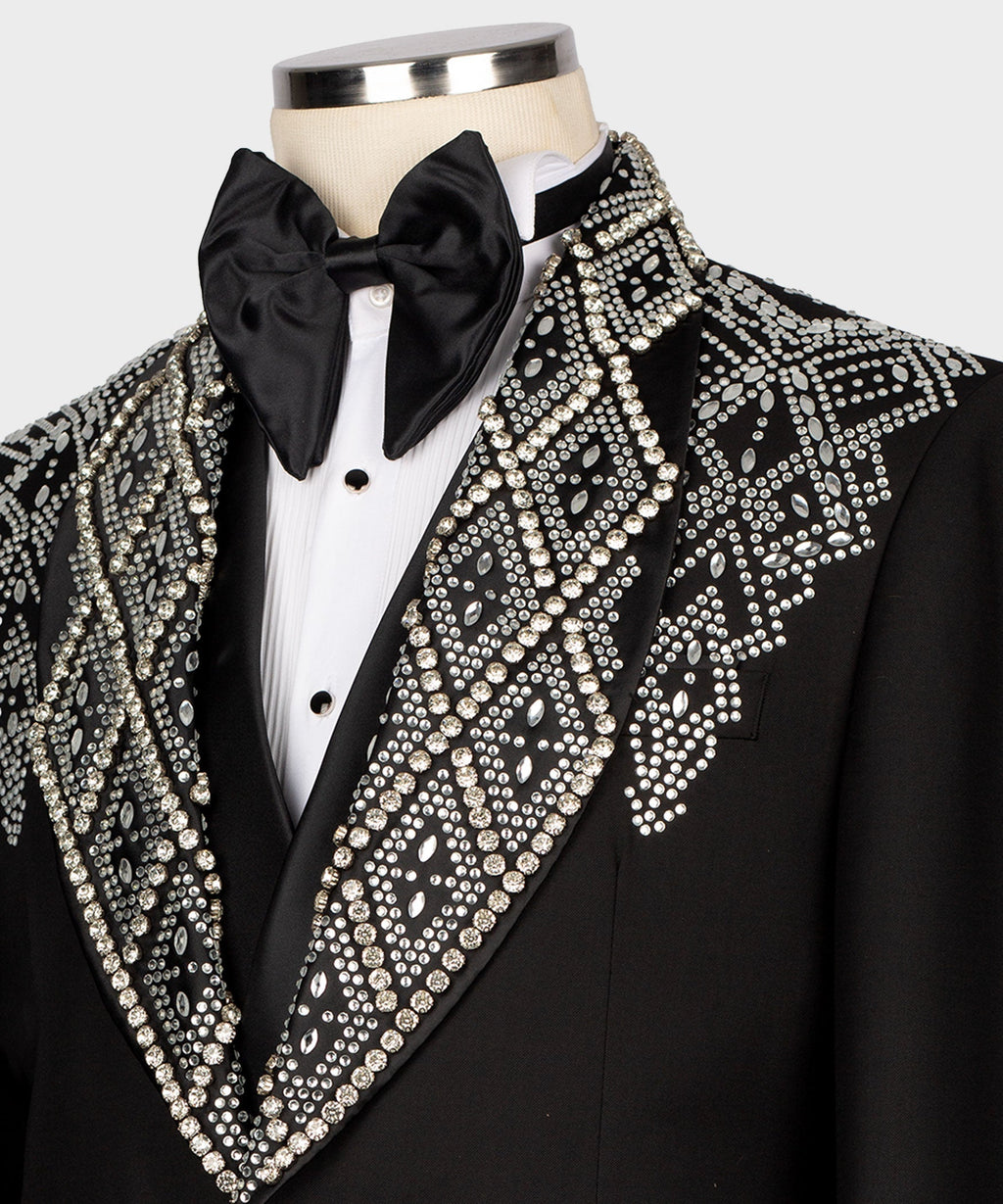 Close-up: black tuxedo lapel with dense rhinestone embroidery over satin trim, bow tie