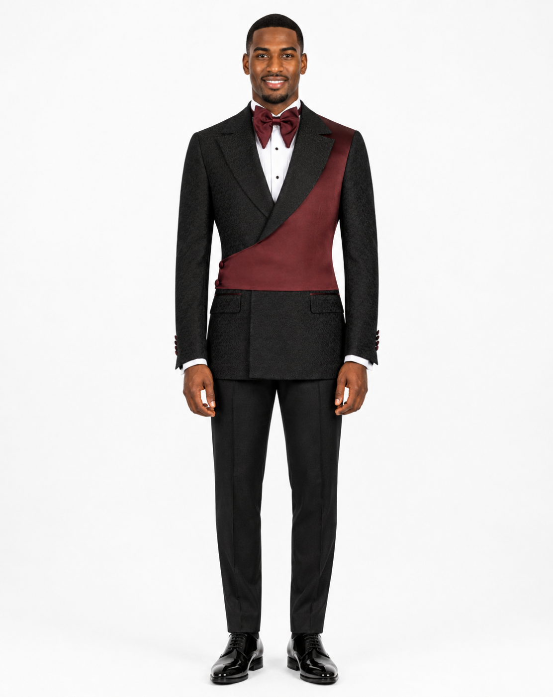 A man modeling a black double-breasted tuxedo with a contrasting burgundy satin peak lapel and matching bow tie