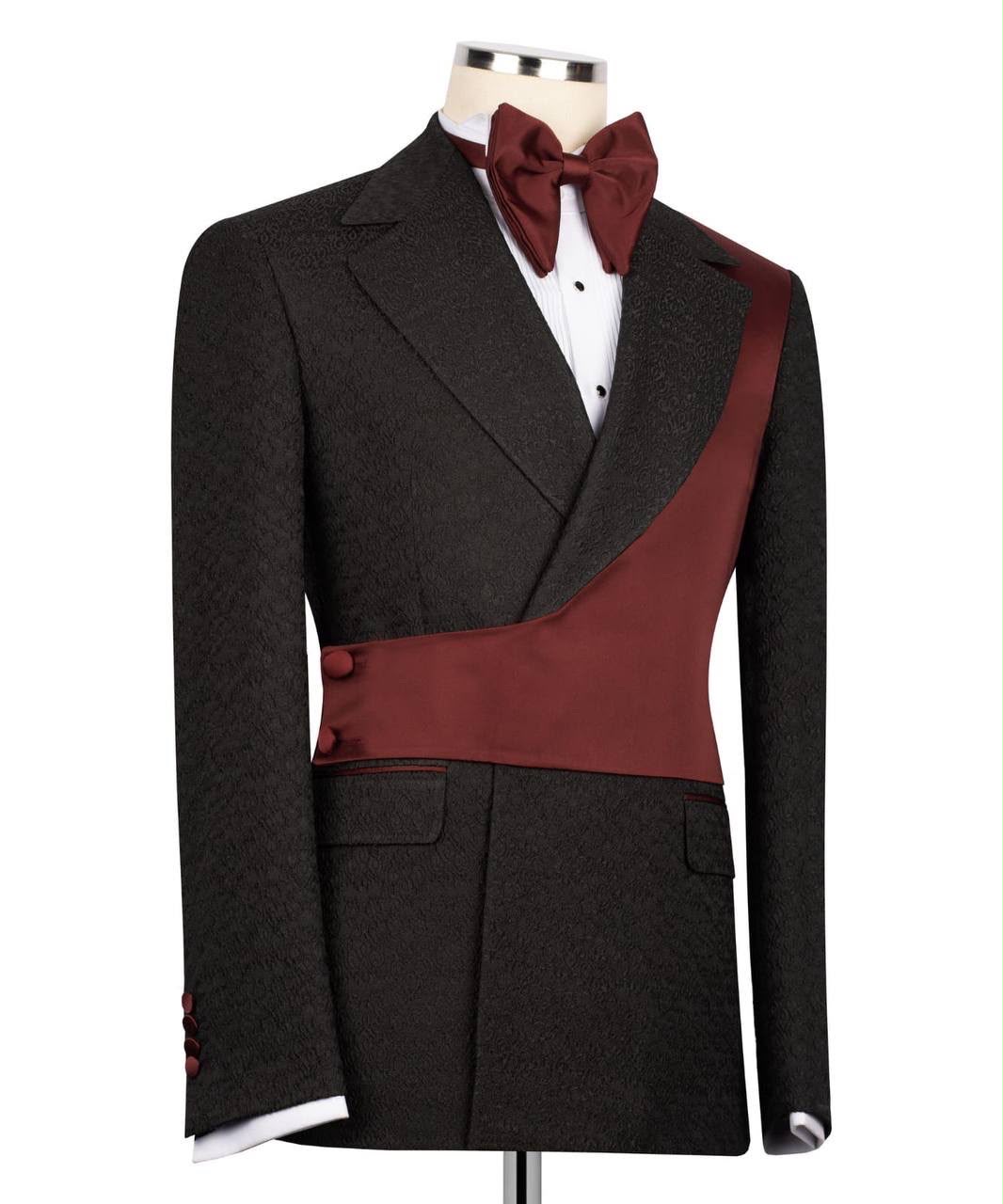 A men's tuxedo jacket displayed on a mannequin torso, featuring a dark charcoal textured fabric body with contrasting deep burgundy satin peak lapels and a matching waist sash, styled with a burgundy bow tie and white dress shirt.