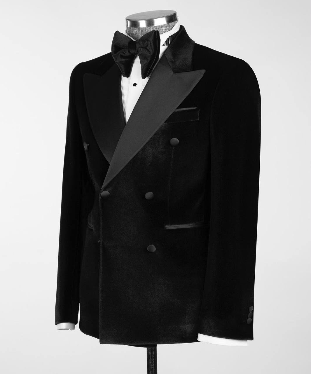 A black double-breasted velvet tuxedo jacket with satin peak lapels, displayed on a mannequin torso with a black bow tie and white dress shirt against a light gray background.