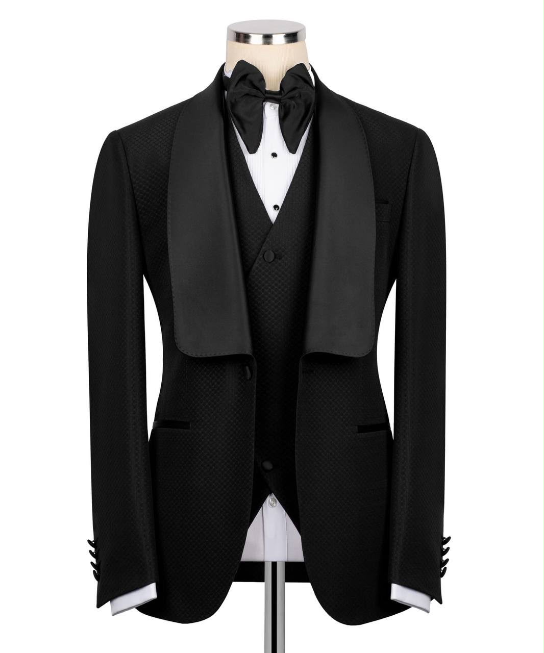 A black tuxedo jacket with satin shawl lapels, displayed on a mannequin torso with a matching black vest, white dress shirt, black bow tie, and white cufflinks 