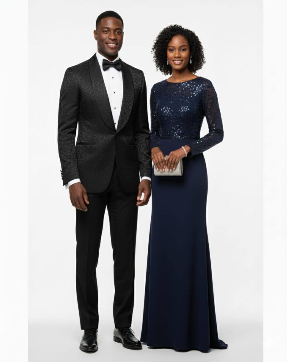 A man and a woman standing side by side in formal evening wear against a light gray studio background. The man wears a black textured tuxedo with a white dress shirt and black bow tie.