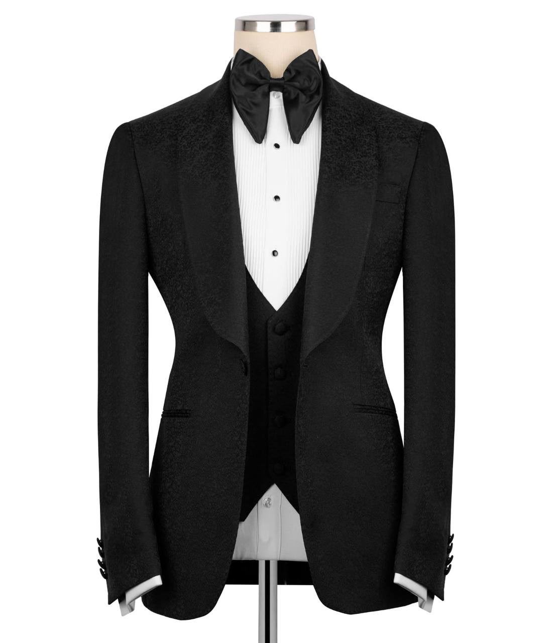 A men's brown textured tuxedo jacket displayed on a mannequin with a white pleated shirt, black bow tie, and matching dark brown vest