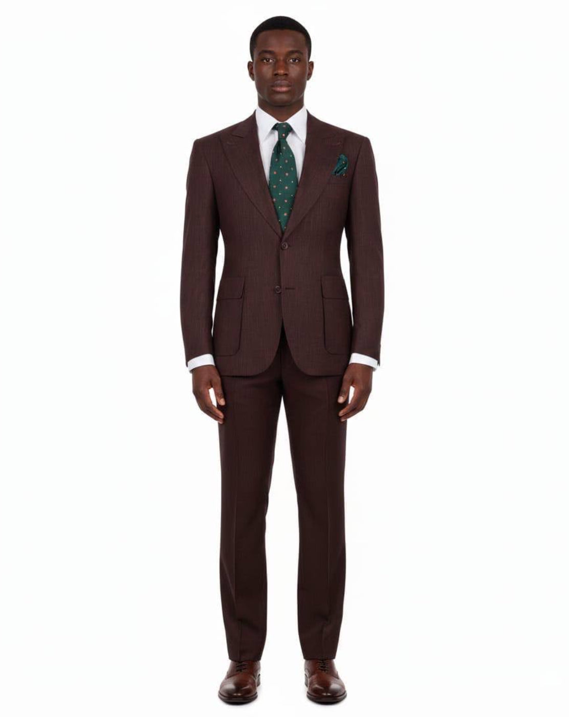 A man modeling a dark brown two-piece suit with a white dress shirt, a green patterned tie, and a green pocket square, standing against a plain white background.