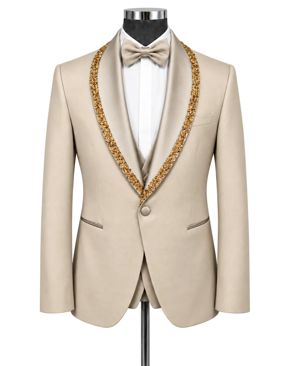 A beige tuxedo jacket with ornate gold beaded trim along the shawl collar, displayed on a mannequin with a white dress shirt, white bow tie, and matching beige vest.