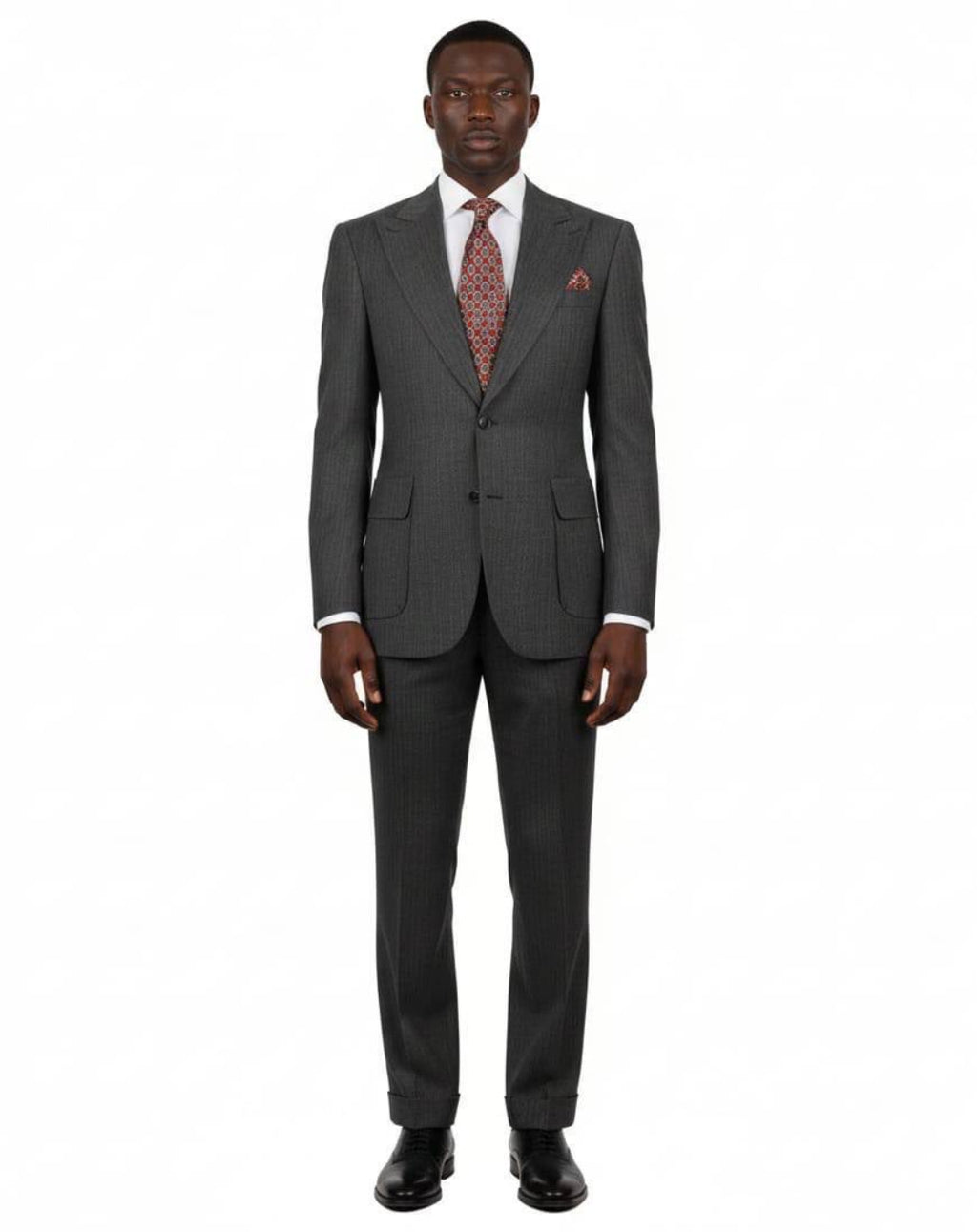 A man modeling a dark gray two-piece suit with a subtle micro-check pattern, paired with a white dress shirt, a red patterned tie, and a matching red pocket square, shot against a solid white background.
