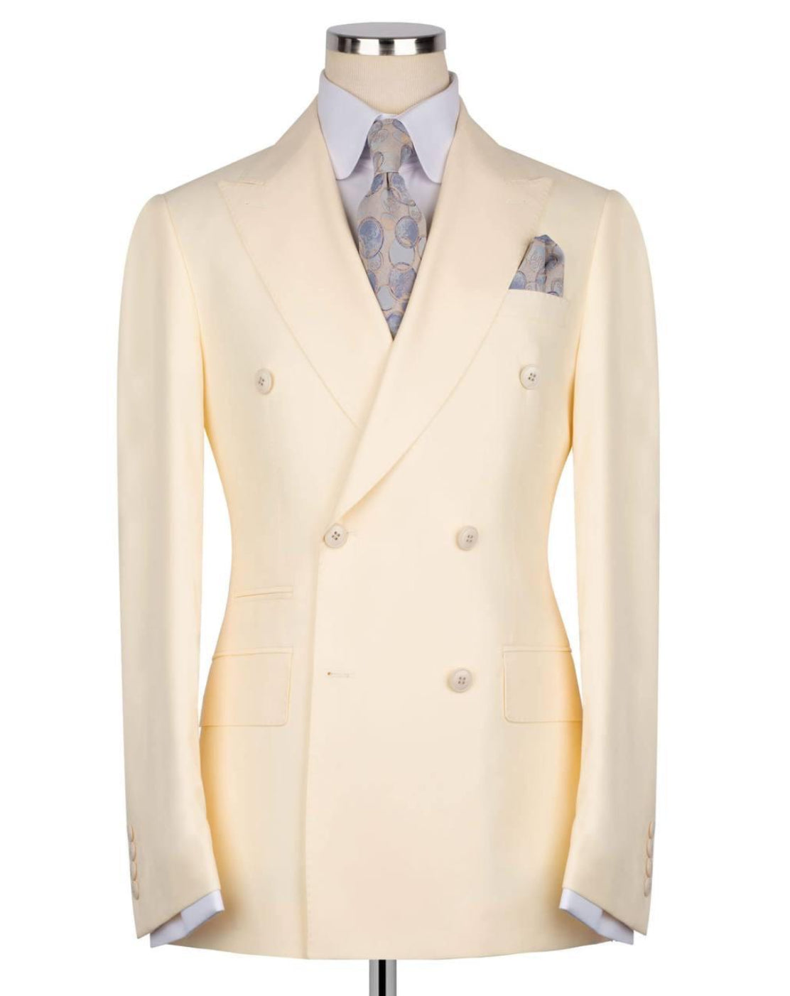 A pale cream double-breasted suit jacket displayed on a mannequin torso, styled with a light blue patterned dress shirt, a matching paisley tie, and a pocket square, set against a plain white background.