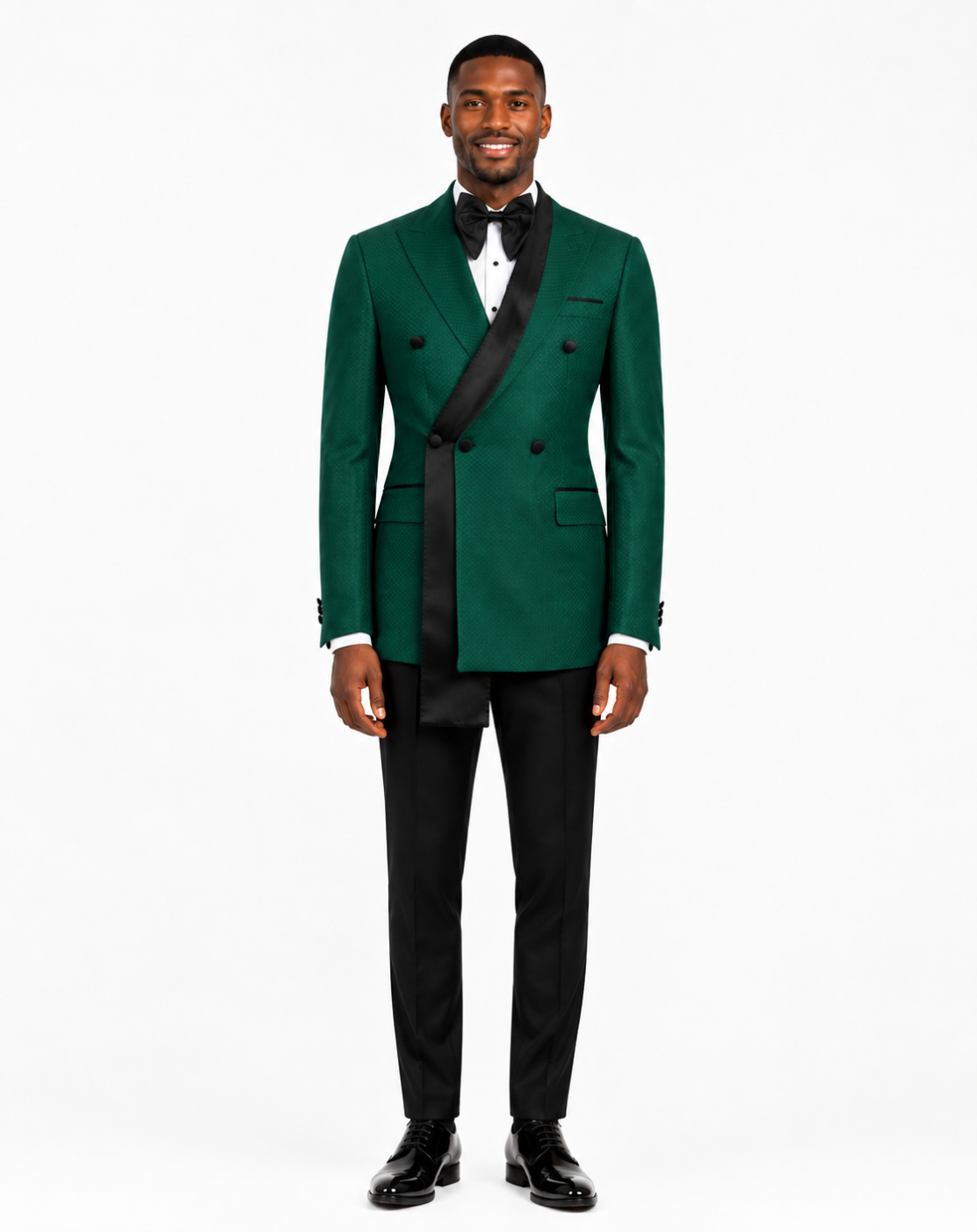 A man modeling a dark green double-breasted tuxedo jacket with black satin peak lapels, paired with black trousers, a white dress shirt, a black bow tie, and black dress shoes 