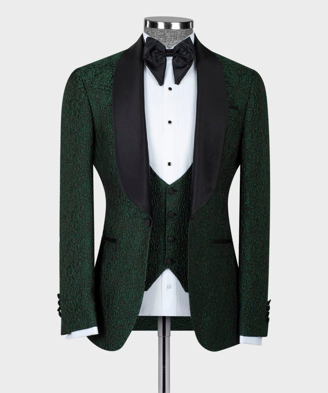 A men's formal tuxedo jacket displayed on a mannequin, featuring a dark green textured jacquard body with contrasting black satin lapels, paired with a white dress shirt, black bow tie, and matching green vest.