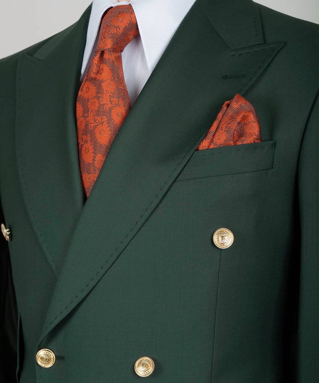 A close-up of a dark forest green double-breasted suit jacket with gold buttons, styled with a white dress shirt, an orange patterned tie, and a matching orange pocket square.