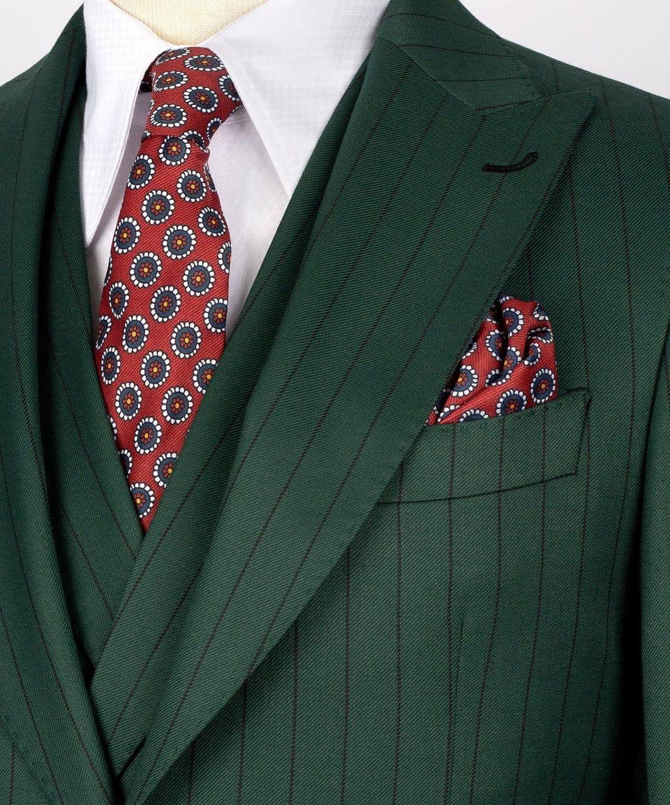 A close-up of a dark green pinstripe suit jacket with a matching red, navy, and white patterned tie and pocket square, worn with a white dress shirt.