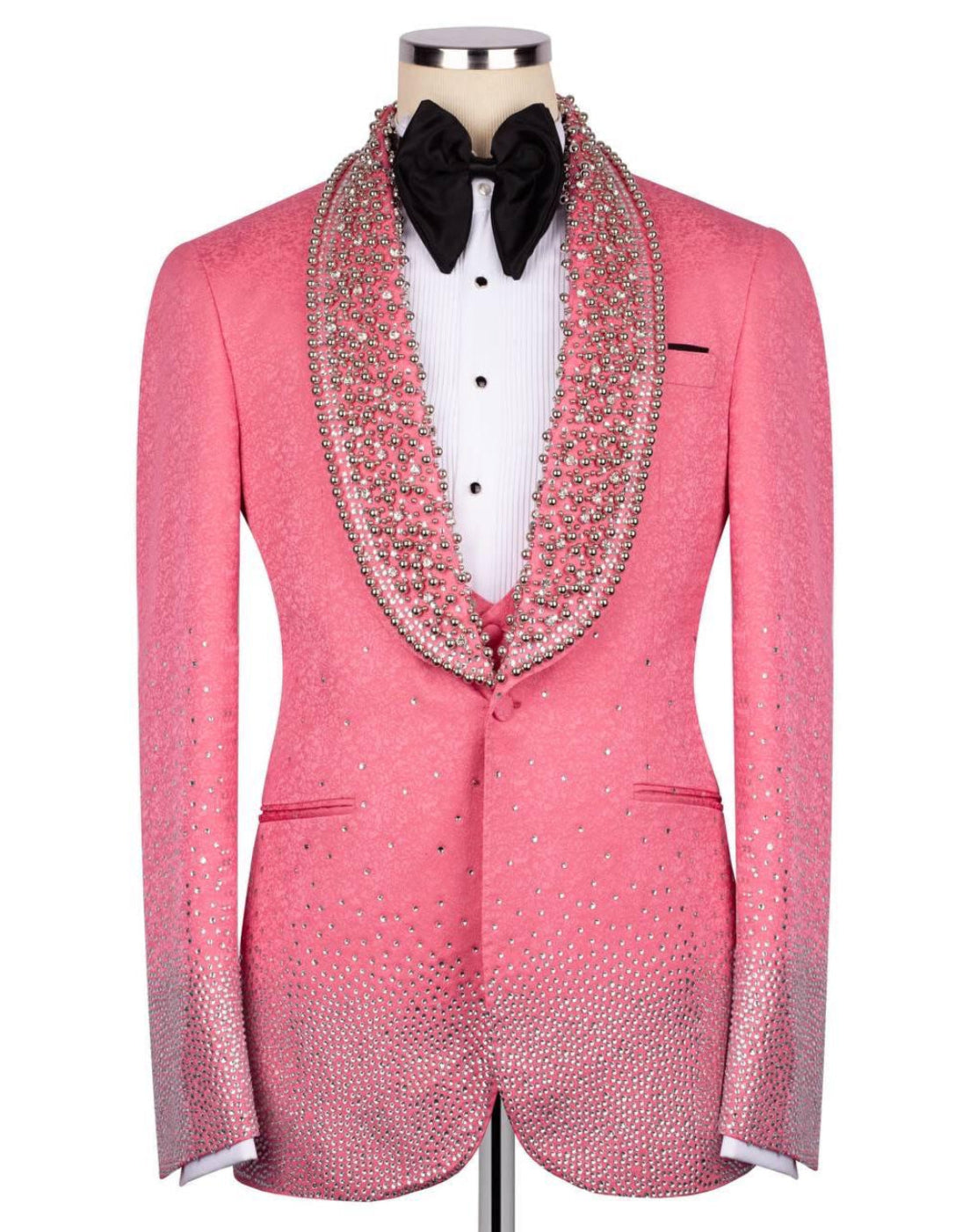 A pink tuxedo jacket embellished with sparkling rhinestones, featuring a wide collar lined with dense rhinestone detailing, displayed on a mannequin with a white shirt and black bow tie.