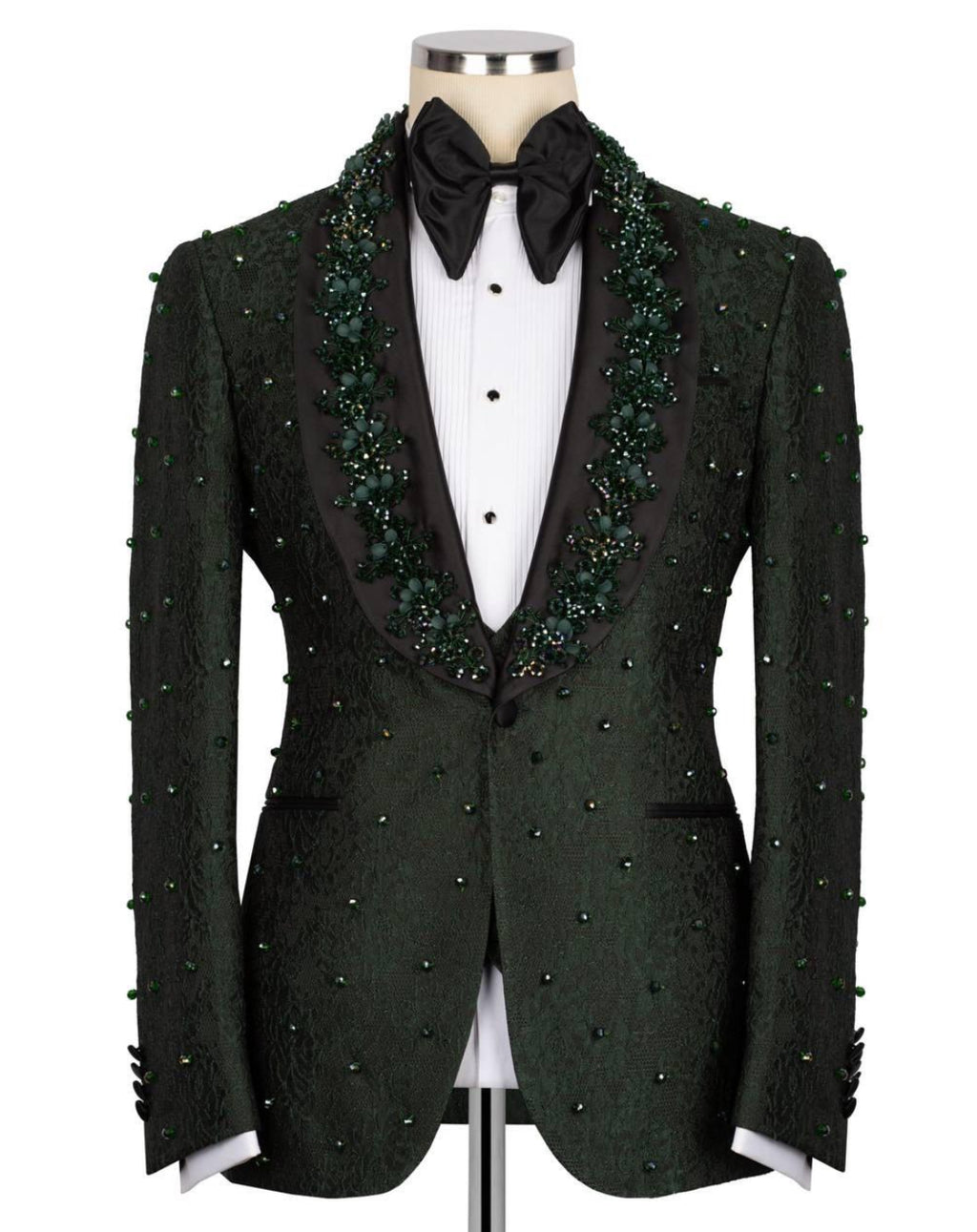 A dark green textured tuxedo jacket with green bead and sequin embellishments, displayed on a mannequin with a black bow tie and white shirt.