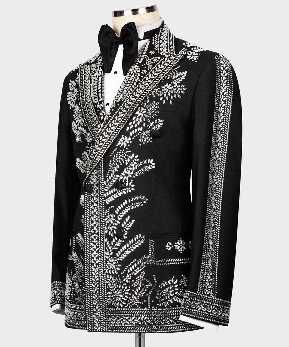 A black men's tuxedo jacket with elaborate silver beaded floral and geometric embroidery, styled on a mannequin with a black bow tie and white shirt against a light gray background.