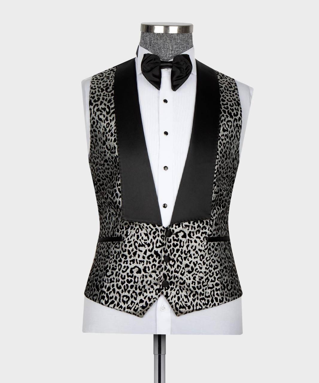 A men's tuxedo vest with a black and gray leopard print pattern and black satin peak lapels, displayed on a white dress shirt and black bow tie mannequin against a light gray background.