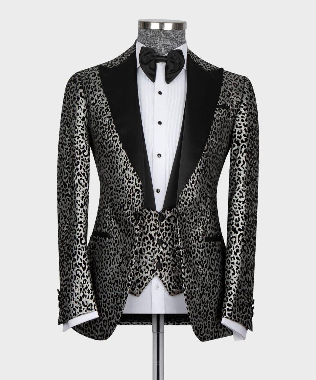 A men's tuxedo jacket with a black and gray leopard print pattern and black satin peak lapels, displayed on a mannequin with a white dress shirt, black bow tie, and white cufflinks.