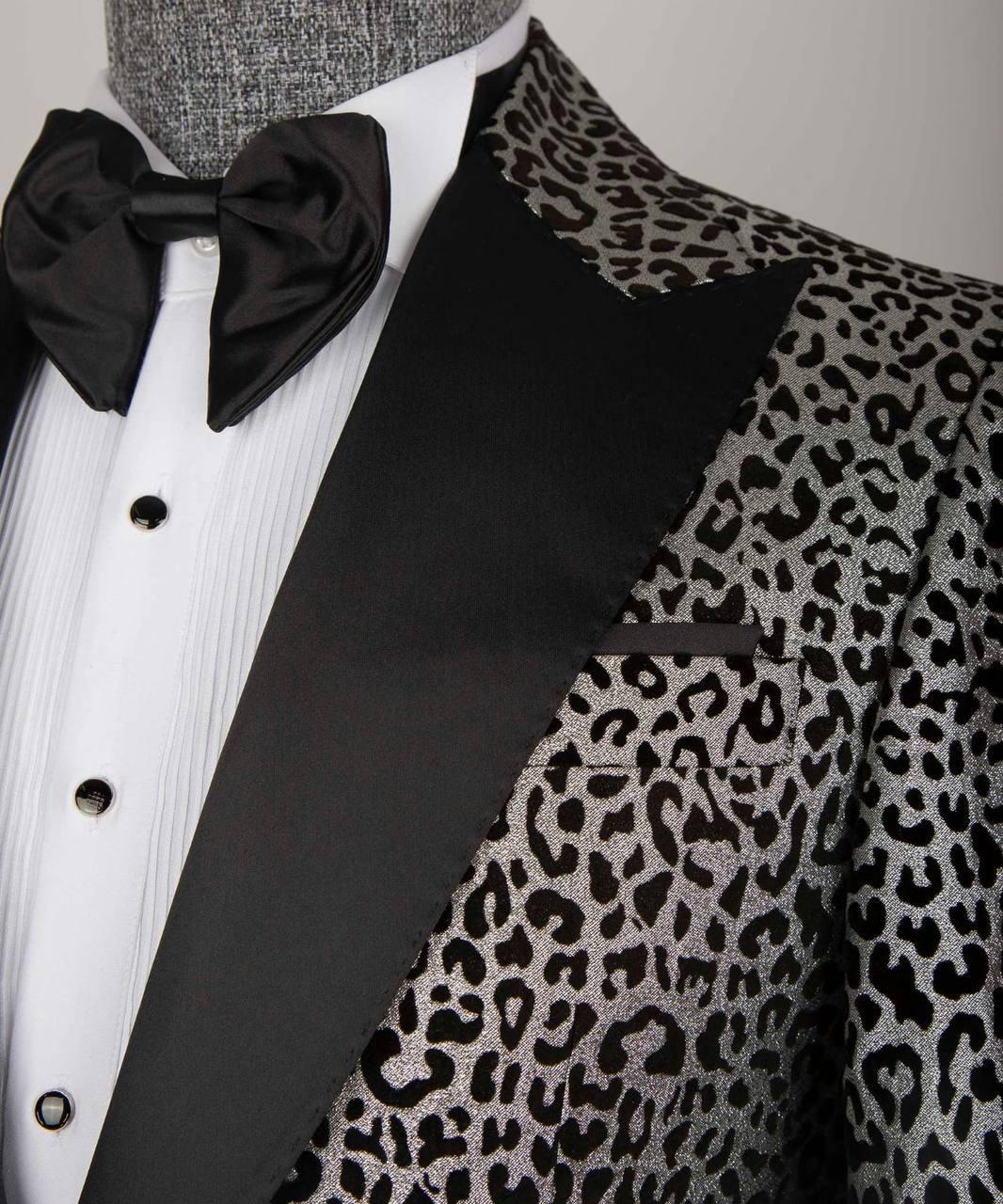 A close-up of a men's tuxedo jacket featuring a black and gray leopard print pattern on the body and lapels, paired with solid black satin peak lapels, a white pleated shirt, and a black bow tie.