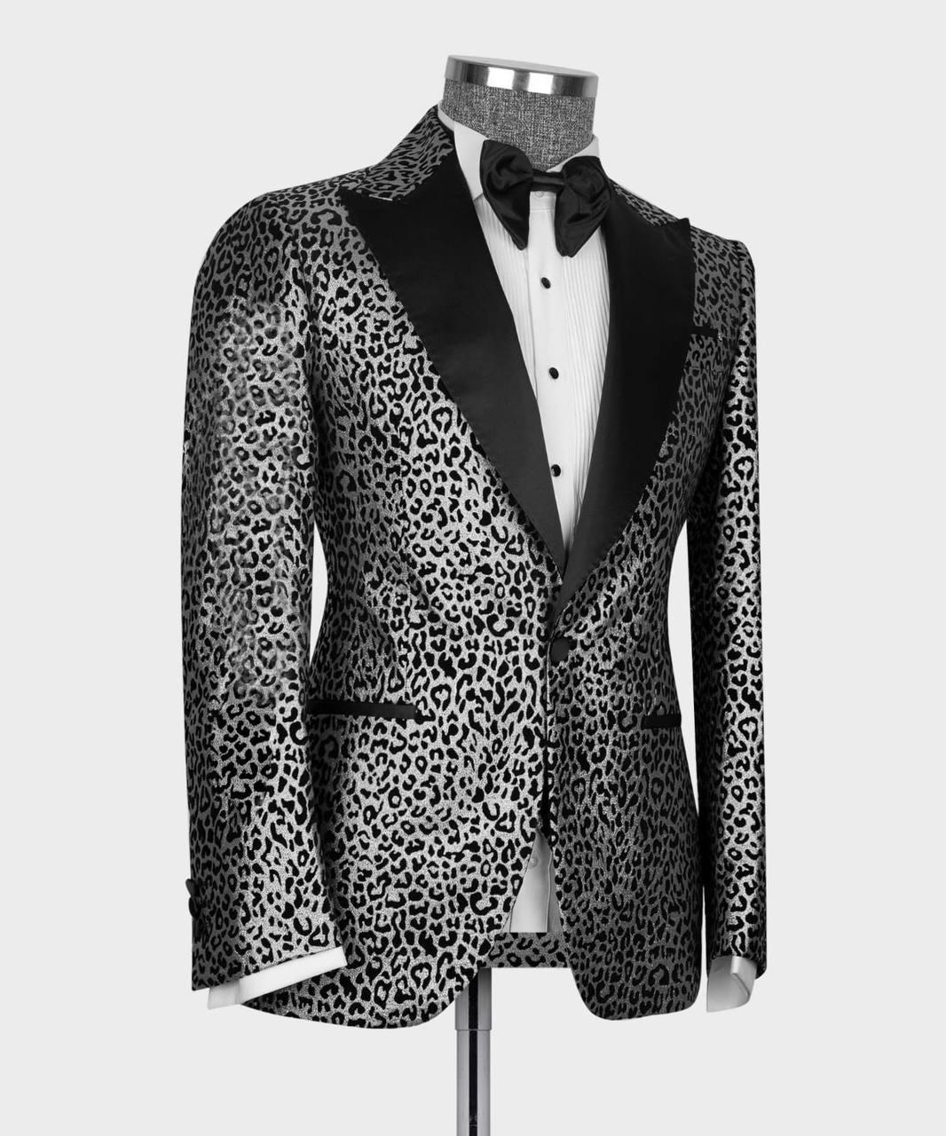 A men's tuxedo jacket with a black and gray leopard print pattern and black satin peak lapels, displayed on a mannequin with a white dress shirt and black bow tie.