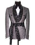 A men's tuxedo jacket displayed on a mannequin, featuring a textured gray patterned body with a wide black shawl collar and matching waist tie adorned with white rhinestones, styled with a white shirt and black bow tie.