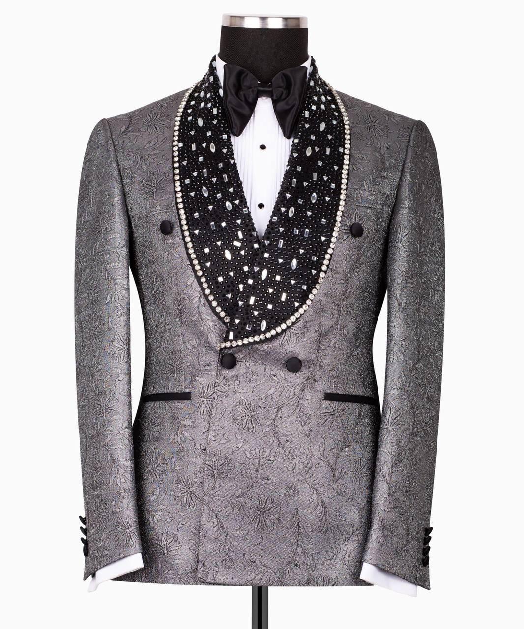 A gray patterned double-breasted tuxedo jacket displayed on a mannequin, featuring a black shawl collar embellished with white pearls and a black bow tie.