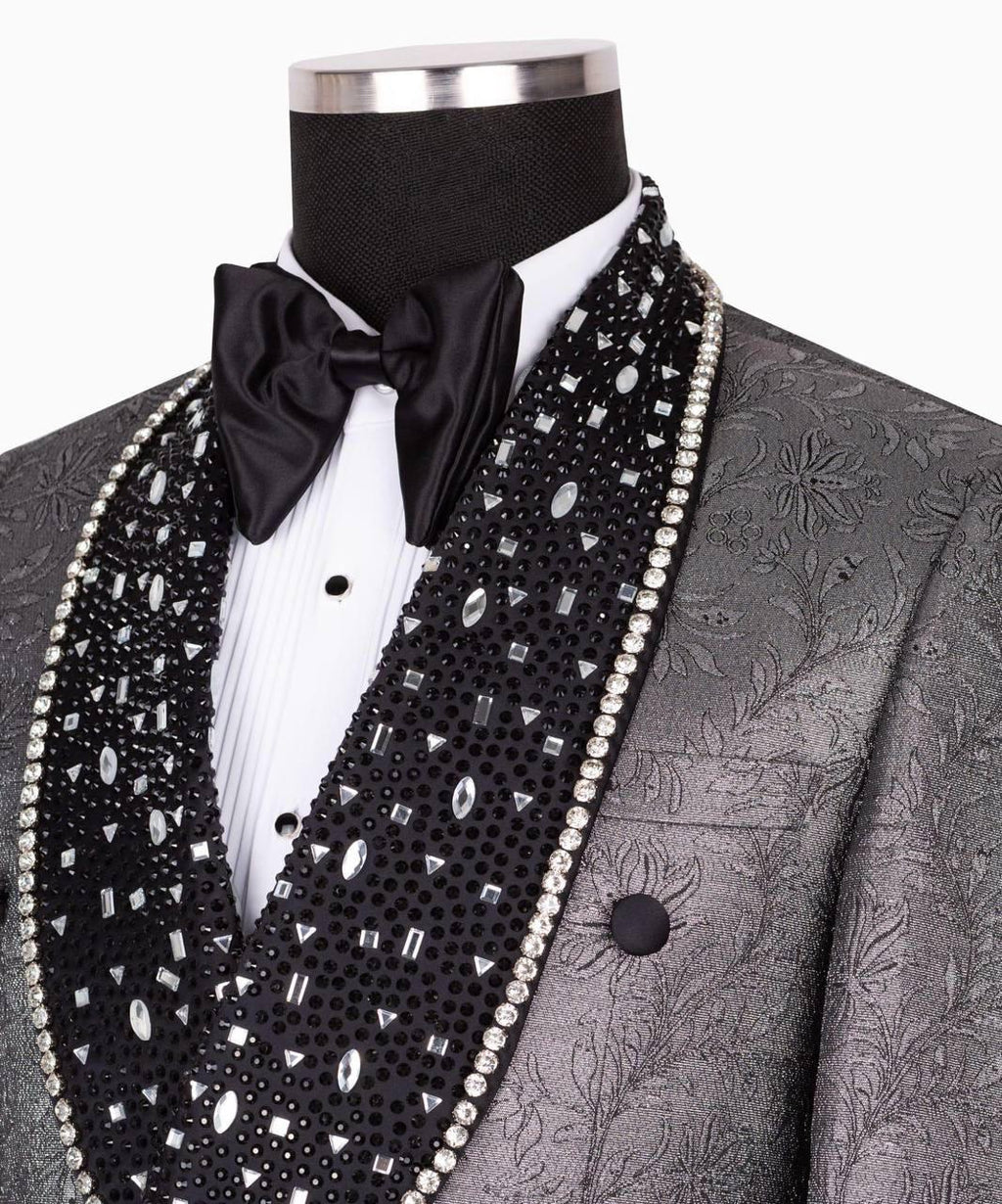 A close-up of a formal tuxedo jacket on a mannequin, featuring a textured gray jacquard body, a black beaded lapel with clear rhinestones and white pearl trim, a white pleated shirt, and a black satin bow tie.