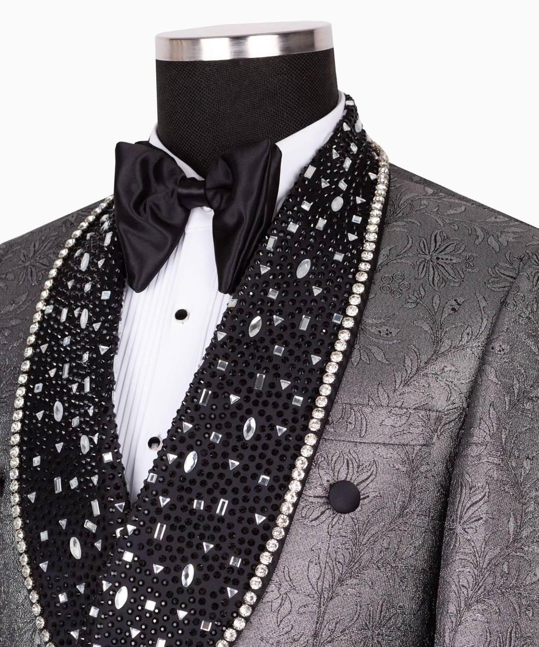 A close-up of a formal tuxedo jacket on a mannequin, featuring a textured gray jacquard body, a black beaded lapel with clear rhinestones and white pearl trim, a white pleated shirt, and a black satin bow tie.
