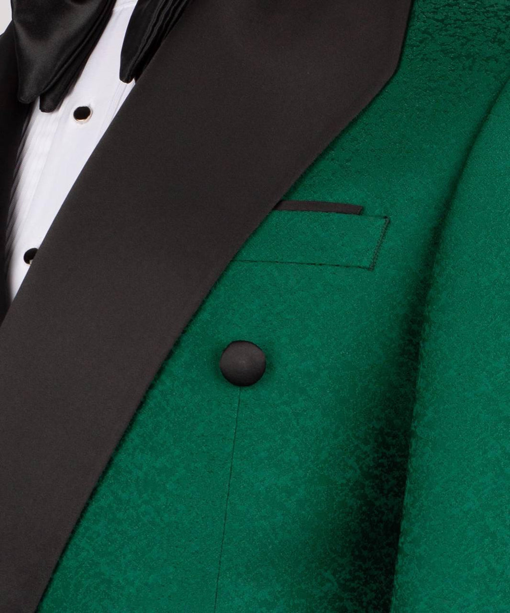 Close-up of a formal tuxedo jacket featuring a rich emerald green textured body with contrasting black satin lapels, a black button, and a white dress shirt with a black bow tie.