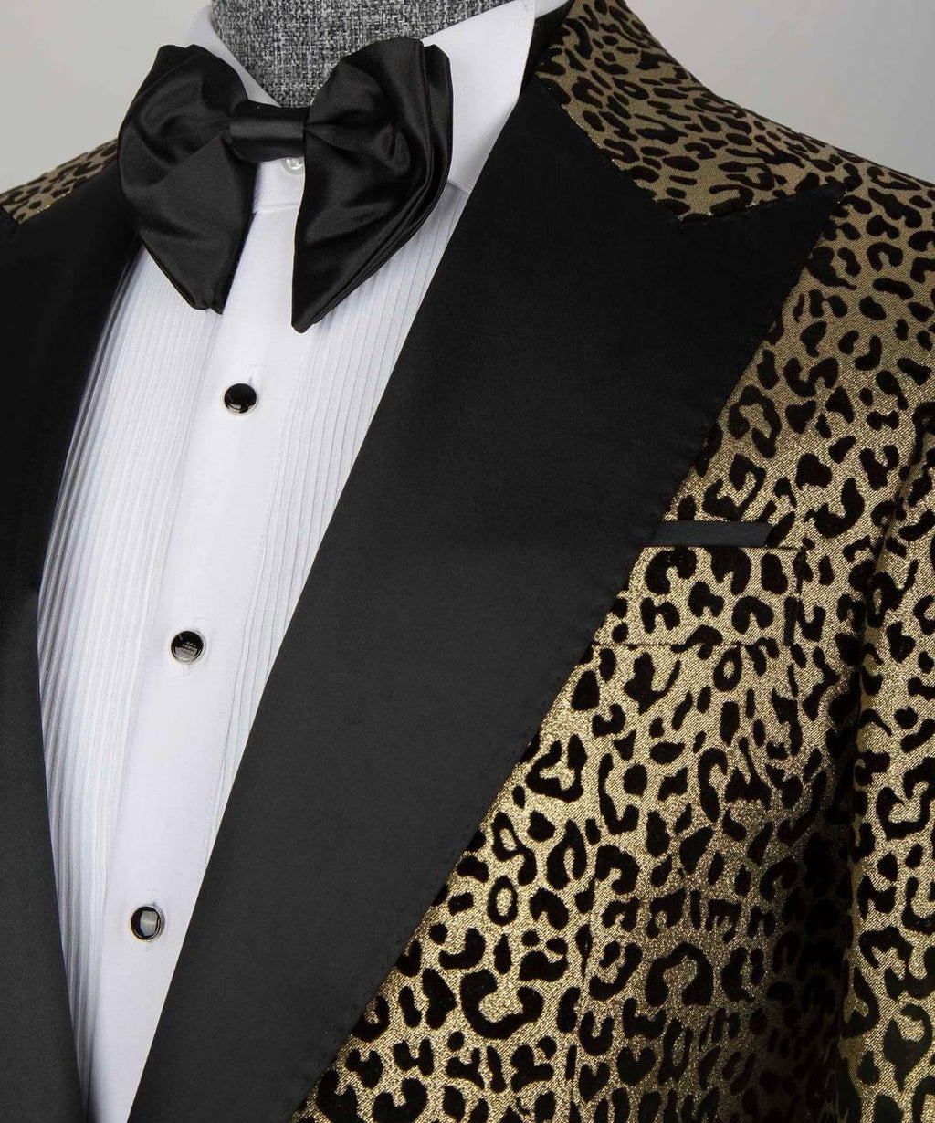 A close-up of a formal tuxedo jacket featuring black satin lapels and a gold leopard-print fabric body, styled with a white pleated shirt and a black bow tie on a mannequin.