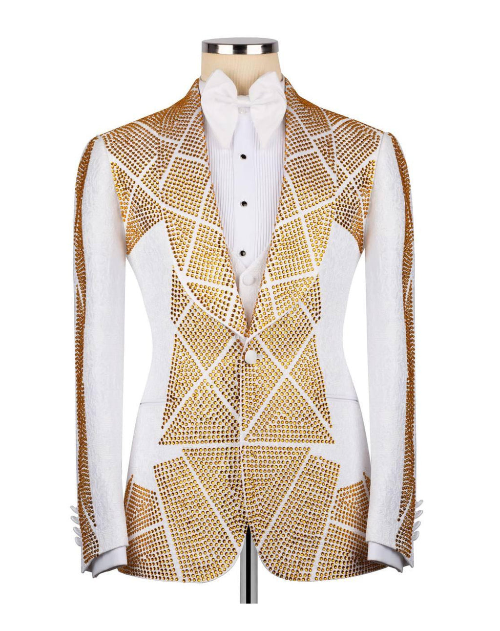 A white tuxedo jacket embellished with gold rhinestone geometric patterns, styled with a white pleated shirt and a white bow tie on a mannequin torso.