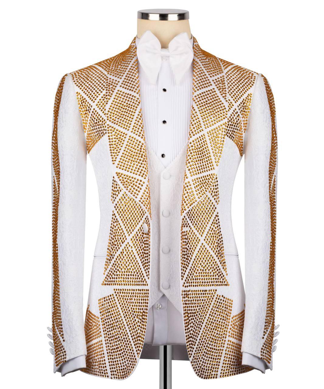 A white tuxedo jacket with geometric gold rhinestone patterns, styled on a mannequin with a white shirt and bow tie against a white background.