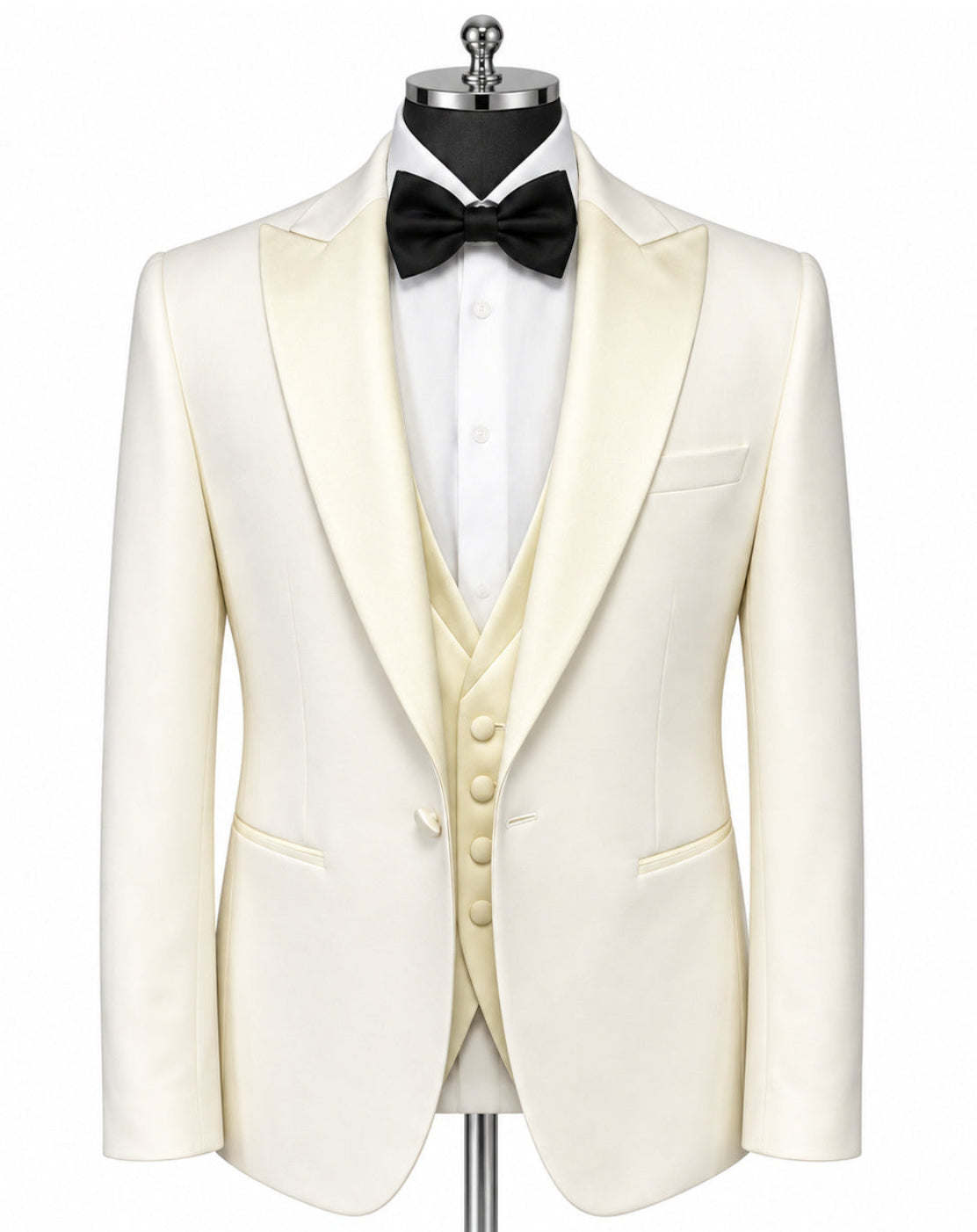 An ivory tuxedo jacket with satin peak lapels, displayed on a mannequin torso with a matching ivory vest, white dress shirt, black bow tie, and a silver stand against a white background.