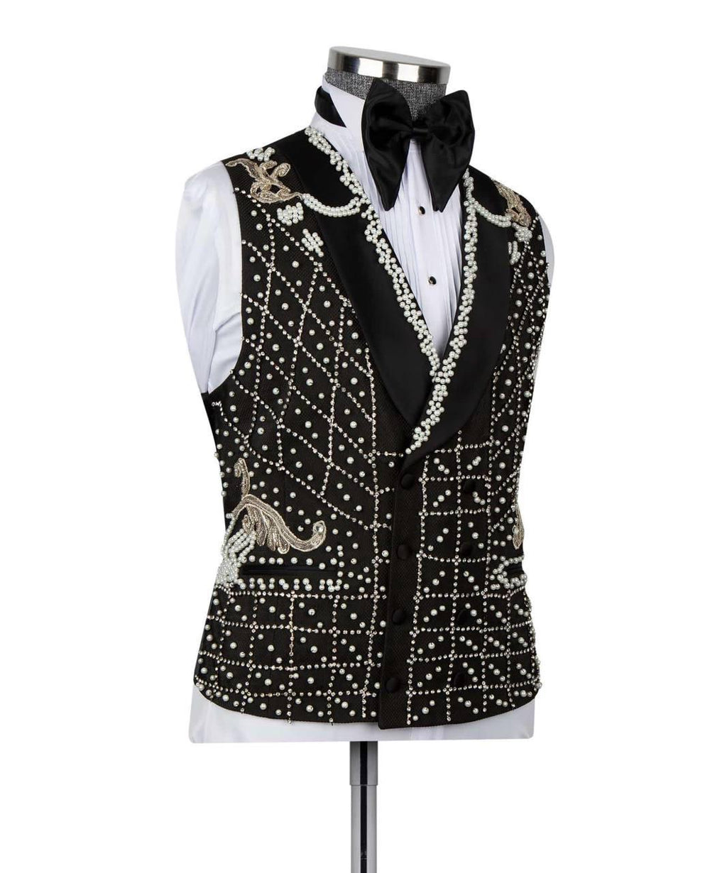 A black velvet tuxedo vest heavily embellished with white faux pearls, silver rhinestones, and gold embroidery, styled on a mannequin with a white shirt and black bow tie.