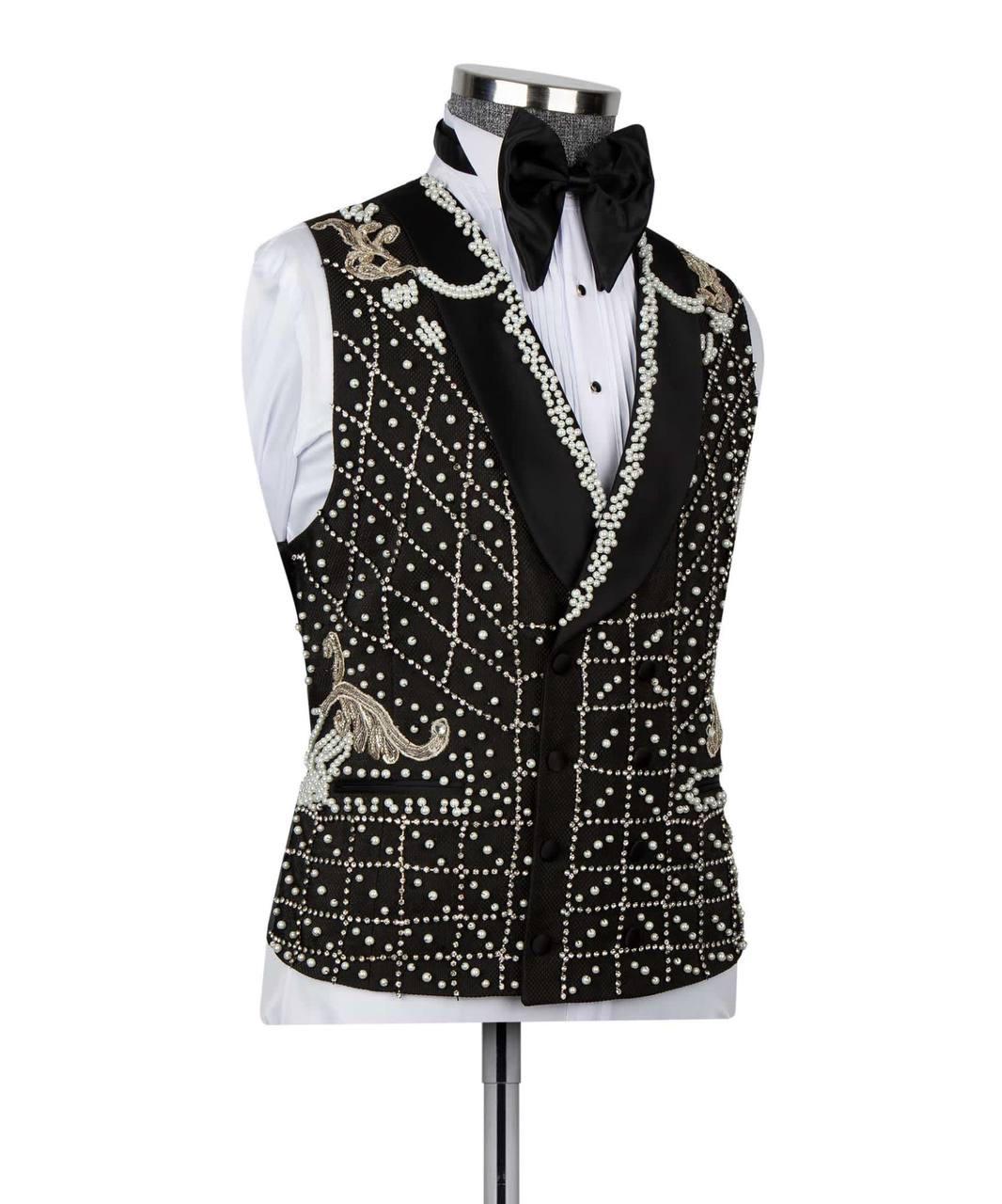 A black velvet tuxedo vest heavily embellished with white faux pearls, silver rhinestones, and gold embroidery, styled on a mannequin with a white shirt and black bow tie.