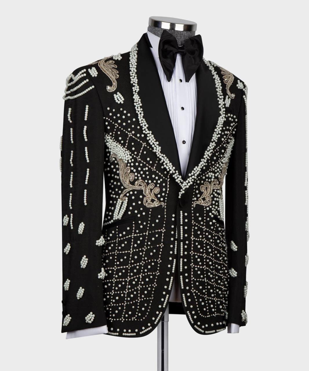 A black tuxedo jacket heavily embellished with white and gold beadwork and embroidery, styled on a mannequin with a white pinstripe shirt and black bow tie against a light gray background.