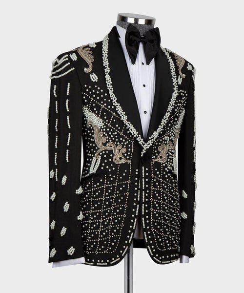 A black tuxedo jacket heavily embellished with white and gold beadwork and embroidery, styled on a mannequin with a white pinstripe shirt and black bow tie against a light gray background.
