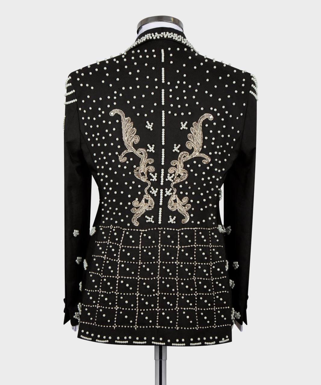 A black embellished jacket displayed on a mannequin, showing the back view with silver rhinestone studs, white embroidered scrollwork, and a white polka dot pattern on a light gray background.