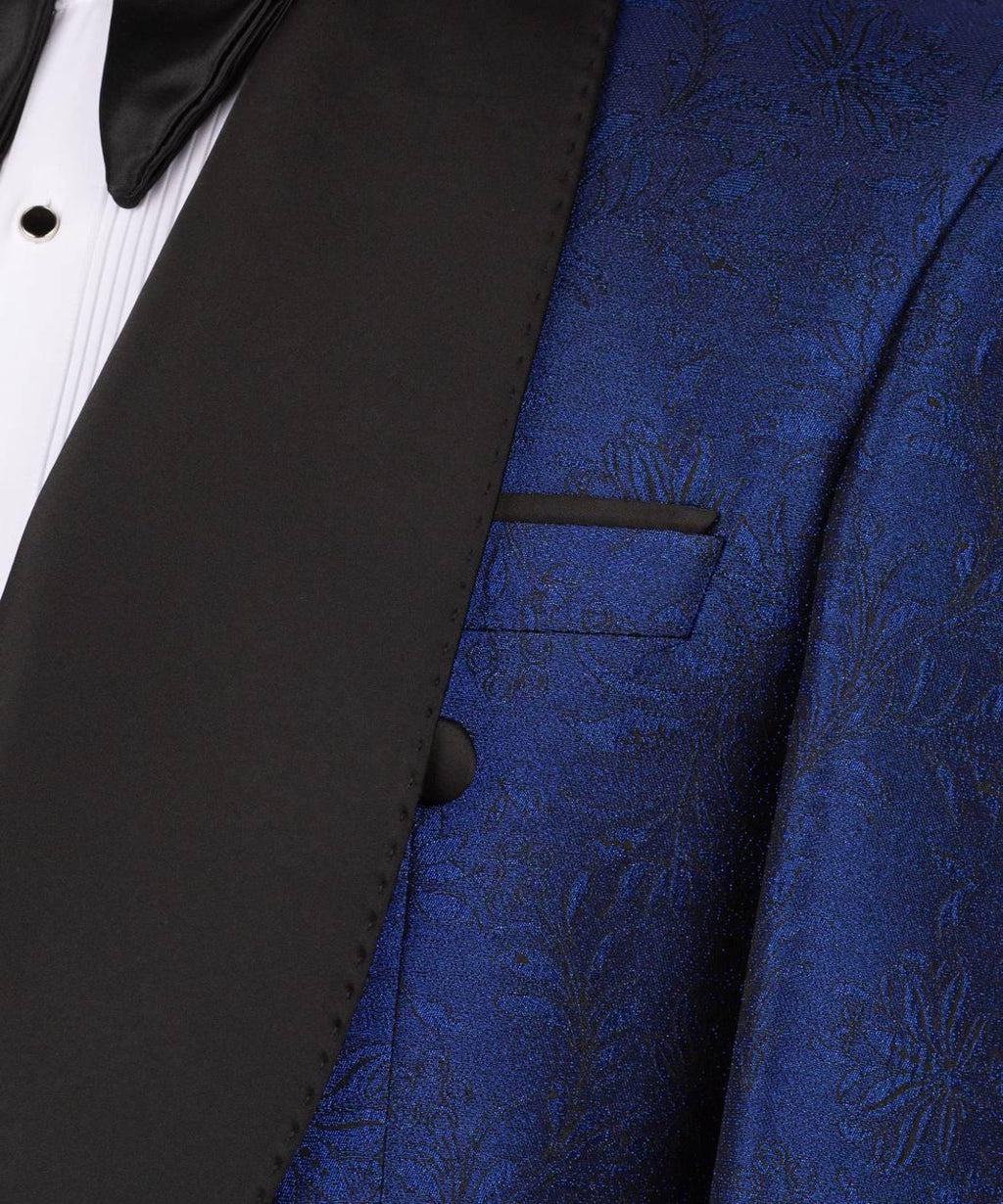 Close-up of a formal tuxedo jacket featuring a rich royal blue brocade patterned vest and a contrasting black satin lapel with a black bow tie and white pleated shirt.
