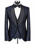 A men's formal tuxedo jacket and vest set on a mannequin, featuring a dark blue and black brocade patterned fabric with contrasting black satin shawl lapels, styled with a white dress shirt and black bow tie.